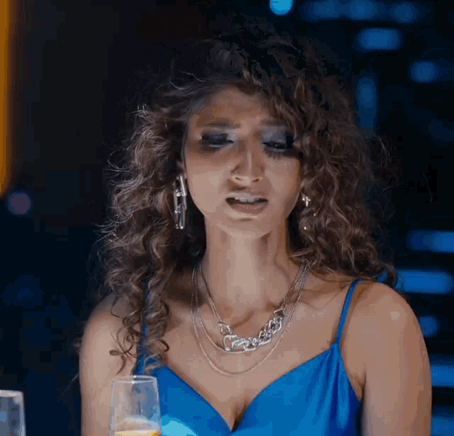a woman with curly hair wearing a blue dress and a necklace that says ' a ' on it