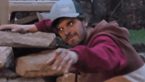 a man wearing a white hat and a red hoodie is reaching out towards a pile of rocks