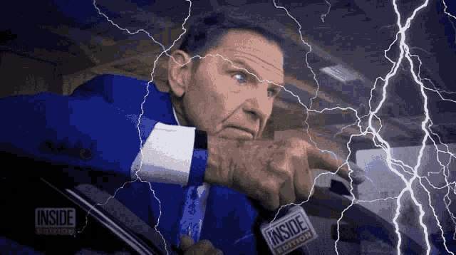 a man in a blue suit and tie is driving a car with lightning behind him