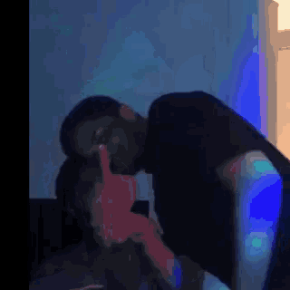 a man and a woman are kissing in a dark room with a blue light behind them