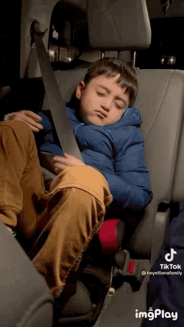 a young boy is sleeping in the back seat of a car while wearing a blue jacket