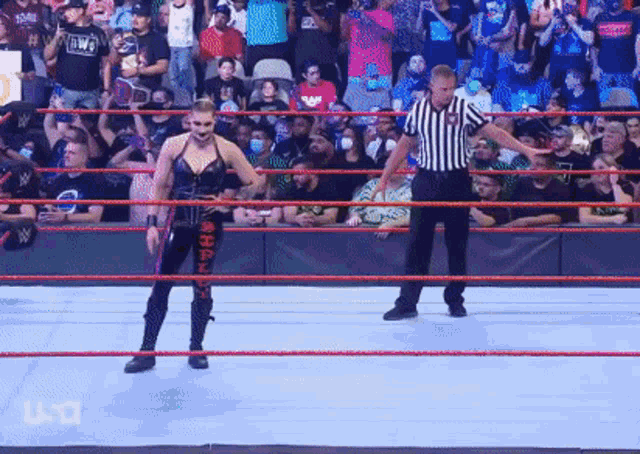 a female wrestler is standing in a wrestling ring with a referee in front of a crowd .