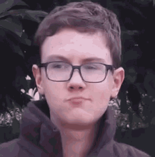 a young man wearing glasses and a black jacket is making a face .