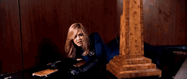 a woman in a blue superhero costume is crawling through a wooden doorway .
