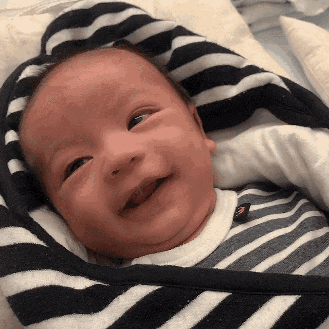 a baby is wrapped in a black and white striped blanket and smiling