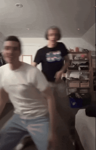 a blurry picture of two men dancing in a room with a shelf in the background .