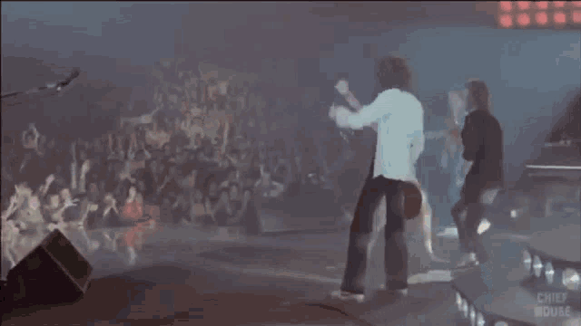 a man without a shirt is singing into a microphone on a stage with a drummer behind him .