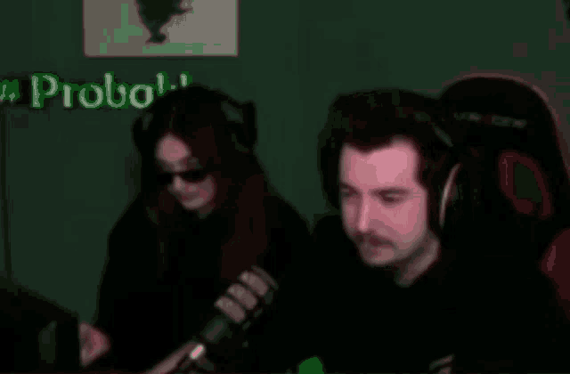 a man and a woman wearing headphones are sitting in front of a microphone in a dark room .