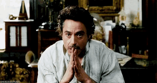 a man in a white shirt is sitting in a room with his hands folded in prayer .