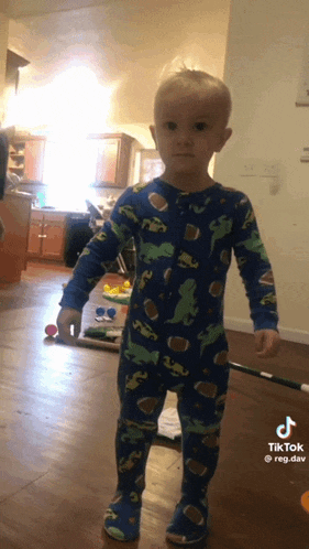 a young boy in a blue dinosaur pajama is standing in a living room