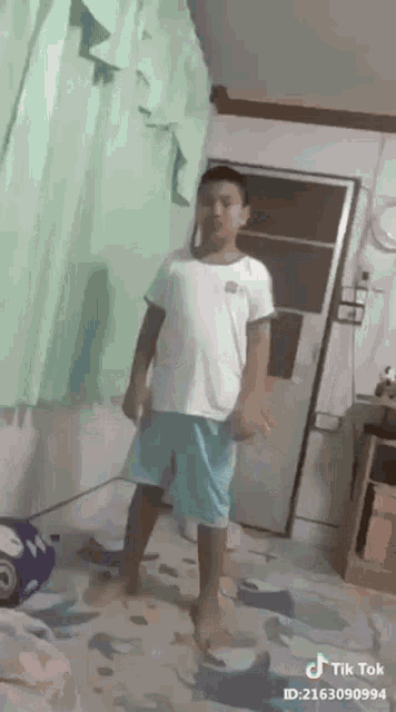 a young boy in a white shirt and blue shorts is standing in a room with a door .
