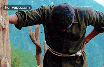 a man is standing on top of a mountain with his arms outstretched and a rope around his waist .