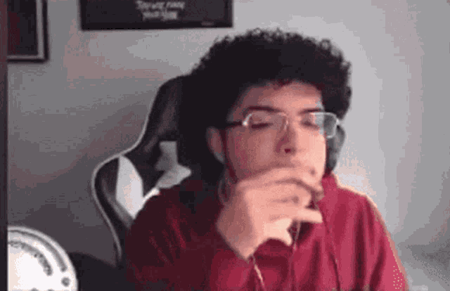 a man with curly hair and glasses is sitting in a chair and drinking from a cup .