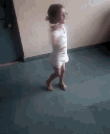 a little girl in a white dress is walking on the floor