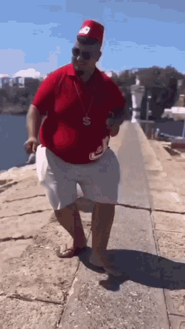 a man in a red shirt and white shorts is walking on a sidewalk near the ocean .