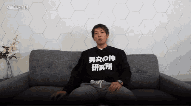 a man sits on a couch wearing a shirt that says ' shimihen tu '