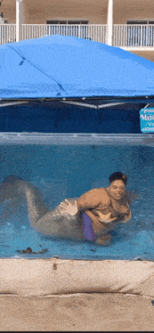 a woman in a mermaid costume is swimming in a pool under a blue canopy
