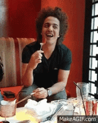 a man with curly hair is sitting at a table with a spoon in his mouth ..