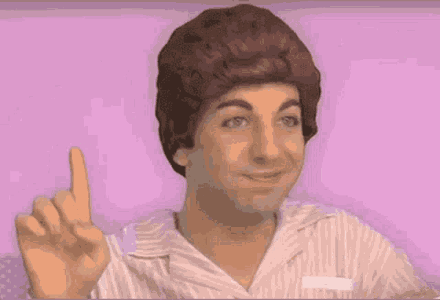 a man wearing a wig and striped shirt points up with his finger