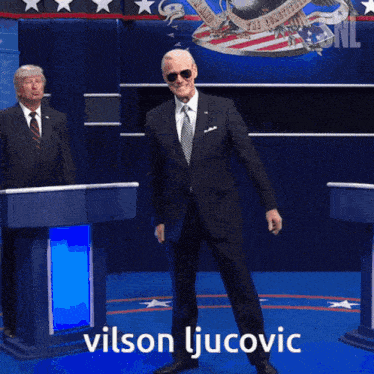 a man in a suit and tie is standing in front of a podium with the name vilson ljukovic written on it