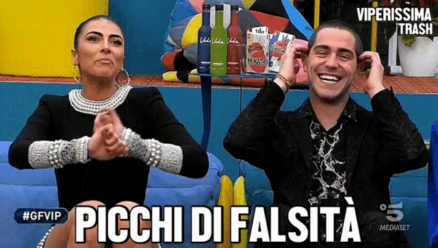 a man and a woman are clapping their hands in front of a sign that says picchi di falsita