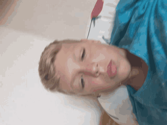 a young boy in a blue shirt is laying on a pillow