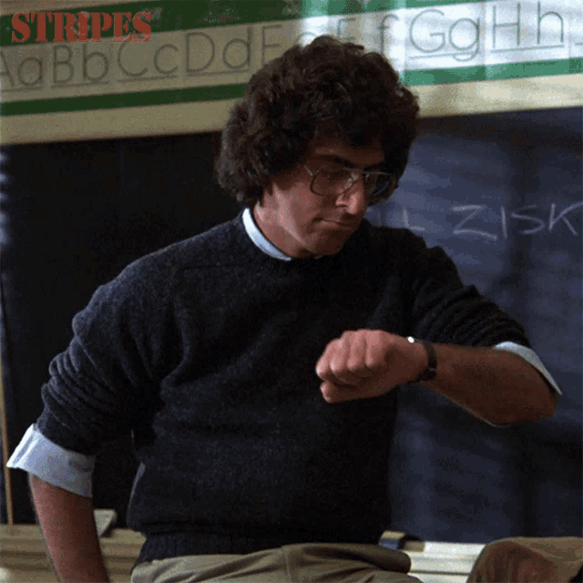 a man is looking at his watch in front of a blackboard with the word stripes written on it