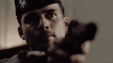 a man wearing a hat with an x on it points a gun at the camera