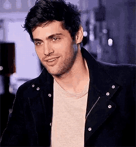 a man with a beard is wearing a black jacket and a white t-shirt .