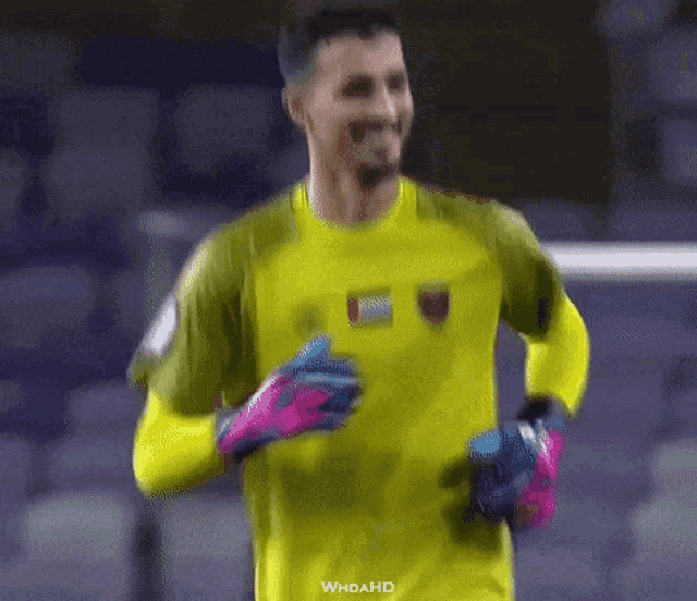 a soccer player wearing a yellow shirt and blue gloves is running on the field .