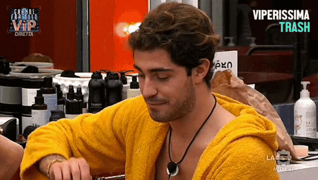 a man in a yellow robe is sitting in front of a tv screen that says viperissima