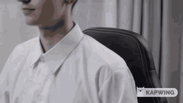 a man in a white shirt is sitting in a black chair with kapwing written on the bottom right