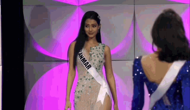 a woman wearing a sash that says myanmar is standing next to another woman .