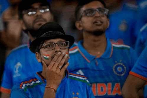 a man covering his mouth with his hand while wearing a blue india shirt