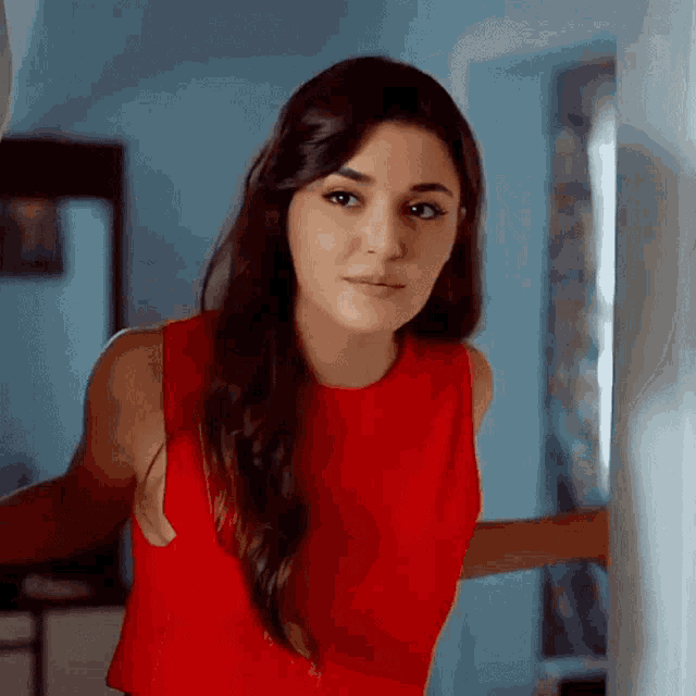 a woman in a red tank top is standing in front of a window .