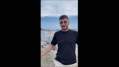 a man in a black shirt and sunglasses is standing on a beach .