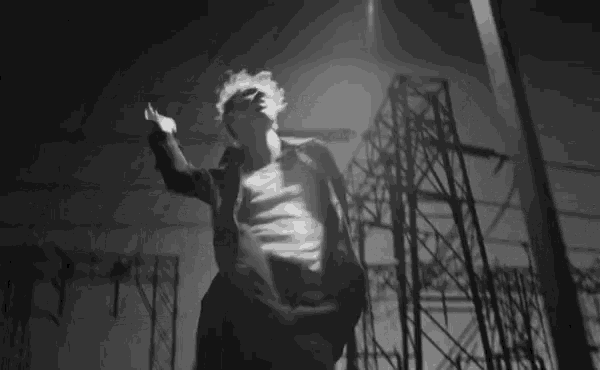 a black and white photo of a man in a suit standing in front of a power plant at night .