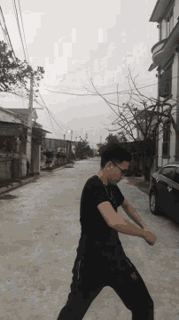 a man in a black shirt with the letter x on his pants is standing on a street