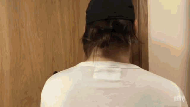 a man wearing a black hat and a white shirt is standing in front of a wooden door