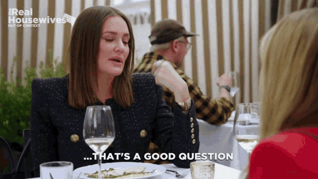 a woman is sitting at a table with a glass of wine and says that 's a good question