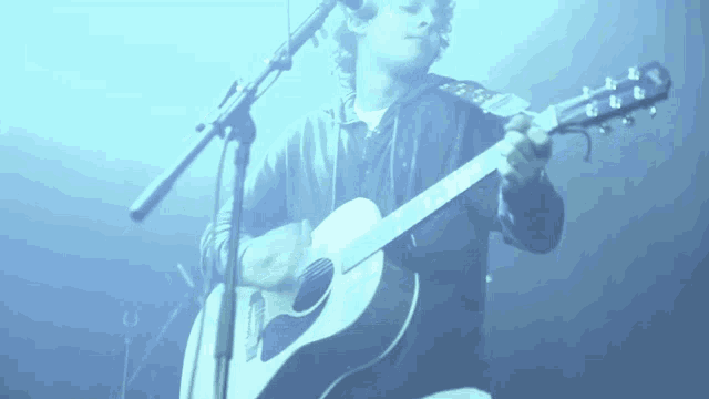 a man is playing an acoustic guitar in front of a blue background