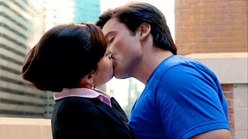 a man in a blue shirt kisses a woman in a pink collar