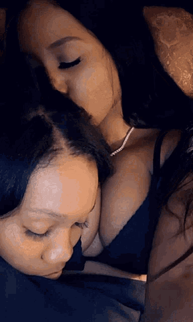 a woman in a black bra is kissing another woman on the cheek