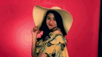 a woman wearing a hat and a yellow dress is standing in front of a pink background .