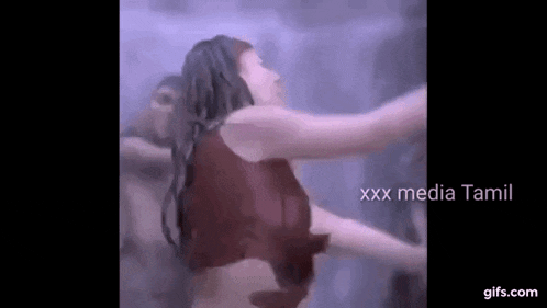a woman in a red tank top is dancing in a dark room with her arms outstretched .