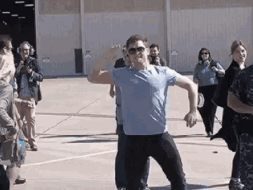 a man in a blue shirt and sunglasses is dancing in front of a group of people .