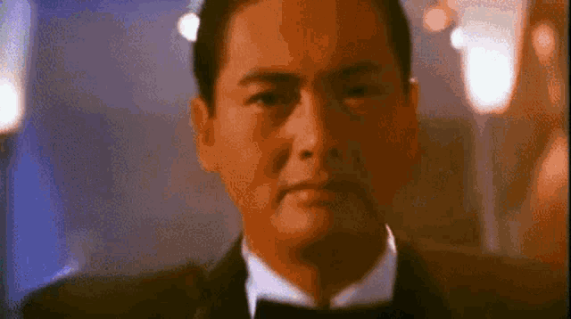 a man in a tuxedo and bow tie is looking at the camera with a serious look on his face .