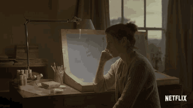a woman sits at a desk with a netflix logo on the bottom right