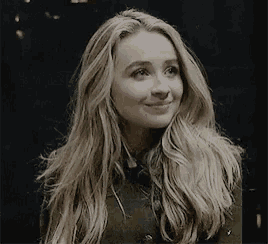a woman with long blonde hair wearing a green jacket is smiling .