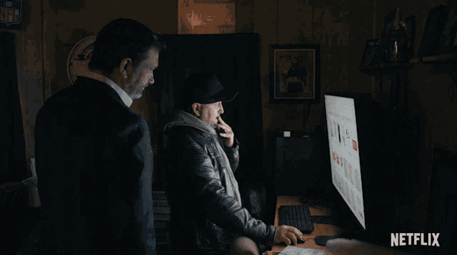 two men looking at a computer screen with netflix written on the bottom right